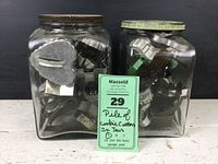 Two glass jars filled with assorted metal cookie cutters, viewed from an angle showcasing a variety of shapes including hearts.