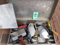 Metal box open showing multiple plastering tools with HYDE branded handles and various sizes of putty knives and scrapers.