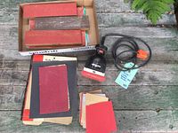 Full view of Porter-Cable sander, box with various sandpaper sheets on a wood surface.