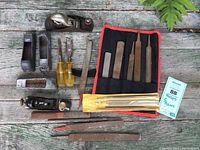 Full set view on weathered wooden surface showing all tools including two metal hand planes, several metal files and rasps, two wood chisels with yellow handles, and fabric roll with files.