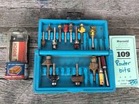 Photo shows full set of router bits in blue storage case and boxed Bosch router bit on left, against wooden background.