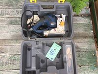 Ryobi biscuit joiner, instruction manual, dust bag, and pack of wooden biscuits in an open plastic carrying case on a wooden surface.