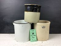 Photo showing the three items: two ceramic crocks and one white enameled pot with black rim. The crocks have a beige finish with a blue crown and "1" logo. The enameled pot shows seams, indicating decorative use only.