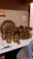 Two large engraved brass trays, one with feet, brass goblets and small cups arranged on tray.