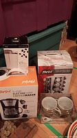 Photo showing boxes of Parini coffee maker, Parisi stainless steel 17-piece carousel spice rack, and individual coffee grinder box with two white ceramic coffee mugs in front.