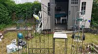 Photo showing two decorative metal garden trellises with round colored glass accents, small tile top table between them, and metal crane bird sculpture beside them on grass near a shed.