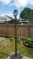 Full view of tall metal plant hanger with three hanging baskets in garden.