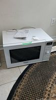 Front angled view of white Panasonic microwave oven on floor with manual on top.