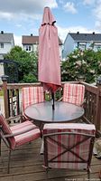 Full view of round glass table with umbrella in center and four chairs with cushions