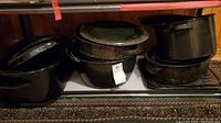 Photo of multiple dark speckled enamel roasters, grill pan, and large pail arranged on a basement shelf
