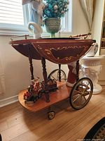 Wooden tea trolley with decorative floral inlay and large wheels in room near window.
