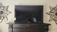 Front view of Sharp Aquos LCD television sitting on a wooden surface, showing the screen and lower bezel with Sharp branding.