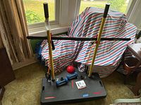 Black balance board with two yellow poles, two blue hand weights, red massage ball, and instructional DVD placed on board