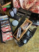 Overall lot contents showing Bose speaker, computer speakers, Craig portable DVD player, assorted DVDs and VHS tapes.