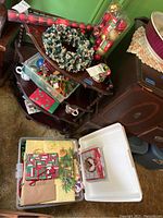 Photo showing a holiday wreath, mugs, giftwrap packages, plastic storage bins, and other Christmas decoration items packed on a wooden tray and floor.