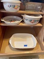 Shelved set of Corelle Abundance stoneware bakeware including covered bakers with lids, open baking dish, pie pan, and clear Corning Ware glass loaf pan.