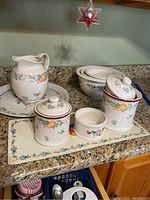 Overall view of ceramic kitchenware on granite countertop showing pitcher, canisters, butter crock, nesting bowls, and decorative tray with fruit motif.