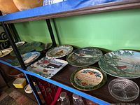 Shelf display of various decorative collector plates in different sizes and designs, including winter scenes and birds.
