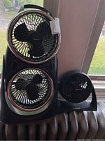Holmes Blizzard single fan and Honeywell double fan standing on radiator by window.