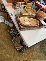 White Lifetime adjustable height folding table with various baskets and miscellaneous items on top, shown folded and standing on carpeted floor.