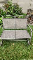 Front view of metal framed patio glider showing woven seat and decorative metal backrest.