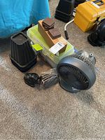 Photo showing black plastic furniture slides, brown and black bed risers, clear plastic toolbox, and gray portable fan on carpeted floor