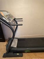 Side view of treadmill showing running surface, handrails, and base structure.