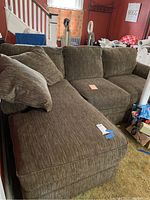 Photo showing left-facing sectional sofa with chaise, textured brown fabric upholstery and matching pillows, situated in living space.