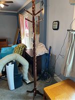 Full view of the wooden coat tree showing carved twisted central column, multiple peg hooks and tripod base.