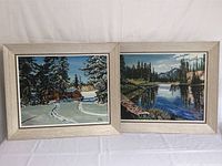 Photo of two framed acrylic paintings by B. Clifton Lemisle, one winter cabin scene and one mountain river landscape, side by side against a white backdrop.