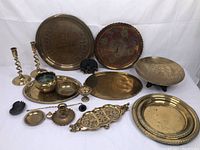 Wide view of the brass lot arranged on white background including platters, bowls, coasters, candlestick holders, and a decorative figure