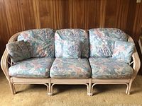 Front view of cane frame couch with floral seat and back cushions and small throw pillows arranged on the couch.