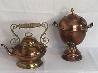 Photo showing copper and brass tea kettle with wooden handle alongside a copper beverage service urn with side handles and spigot.
