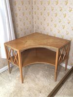 Full view of wooden corner table placed in a corner with floral wallpaper background and carpeted floor.