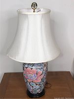 Full view of the ceramic lamp with white fabric shade on wooden surface, showing overall shape and size.
