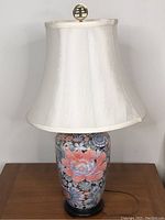 Full view of porcelain lamp base with colorful lotus flower design and white fabric lampshade