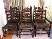 Full front view of six vintage wooden dining chairs with cane seats arranged side by side showing both side and captain chairs.