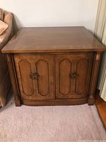 Full front view of vintage wooden end table with cabinet doors and decorative hardware handles.