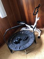 Photo shows Healthware Row-N-Ride rowing machine next to Needak exercise trampoline with two black hand weights placed on trampoline.