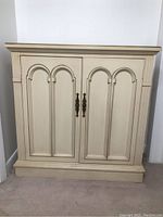 Front view of the hall cabinet showing decorative arched panels on two doors and brass handles.