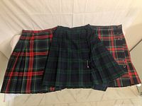 Lot of three kilts laid flat showing various tartan patterns and colors