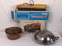 Stacked items showing Norjac French bread warmer in original box, Pyrex oblong baking dish in box, Corning amber glass covered pot, and stainless steel chafing dish with lid.
