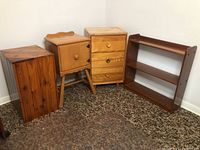 View of four wooden furniture pieces grouped: small bookcase, three drawer dresser, storage cabinet, and hollow side table.