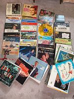 Top view of assorted vintage vinyl records spread on floor showing album covers with various artists including Bing Crosby and musical titles.