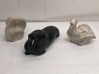Three small stone carvings on a white background: abstract pale stone, black walrus sculpture, and white-gray bird sculpture.