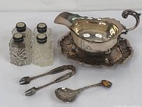 Full view of salt and pepper shakers, gravy boat on platter, and serving utensils arranged together.