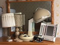 Photo depicting two vintage table lamps and the Clairol True-To-Light VIII lighted makeup mirror along with the General Electric travel iron and Lady Kenmore hair dryer on a wooden dresser.