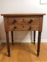 Full front view of the vintage wooden nightstand showing two drawers with wooden knobs and keyholes, and four turned legs.