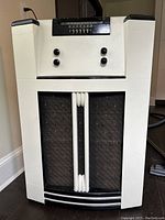 Front view of the antique radio showing the cream-colored body, black speaker grille with vertical white accents, and overall shape.