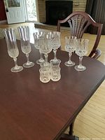 First photo showing several crystal stemware items including champagne flutes, wine glasses, and short tumblers on a wooden table.